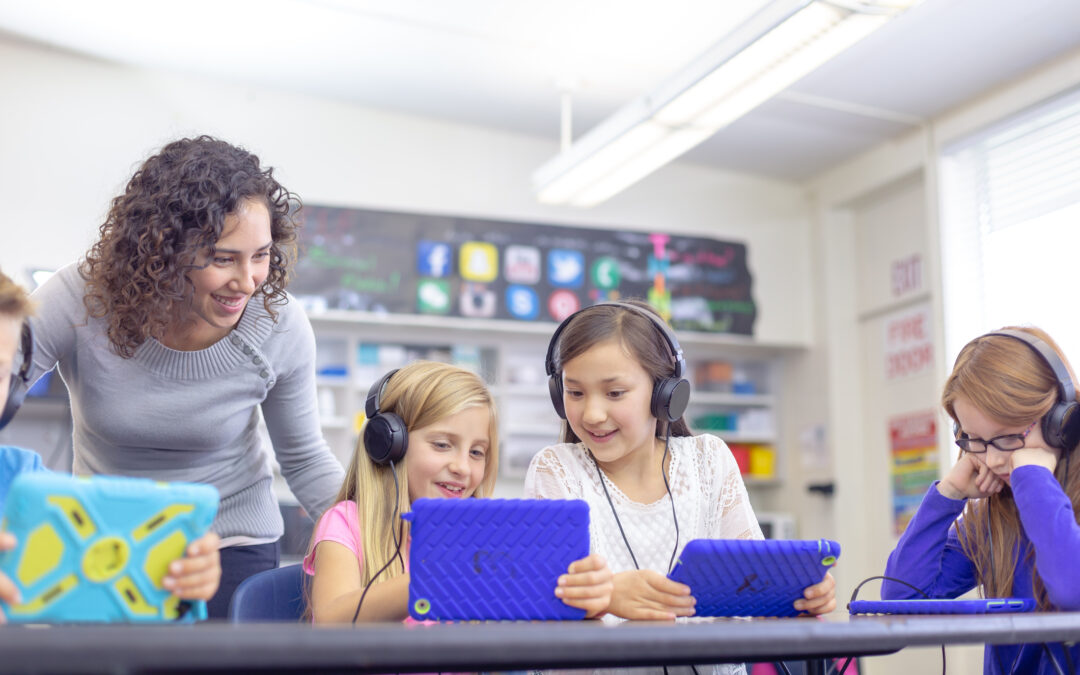 Teacher in classroom with elementary students looking at tablets discussing classroom netiquette