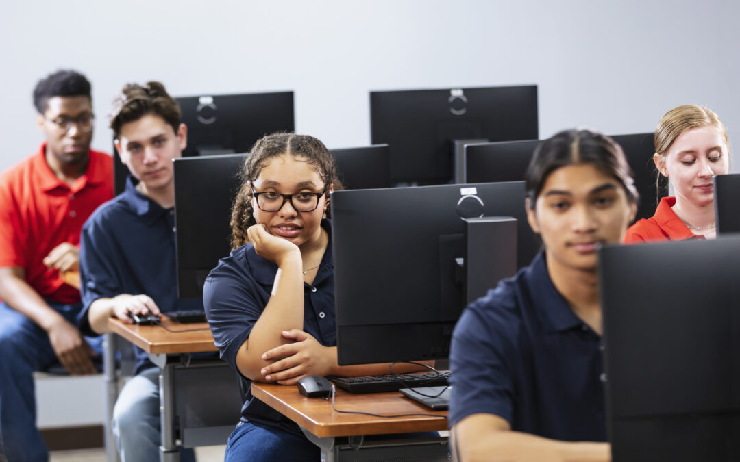 Diverse middle school technology classroom with students in front of computers looking at camera as they learn technology literacy