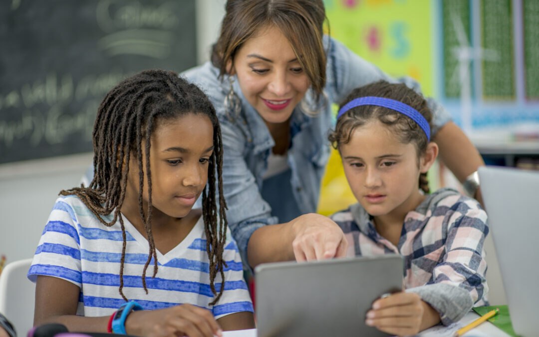 Teacher helping two students learn to code on tablet in classroom