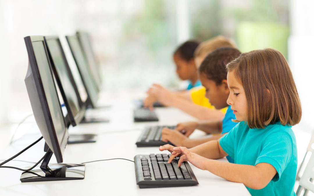 Four young students at desktop computer learning keyboarding skills at young age