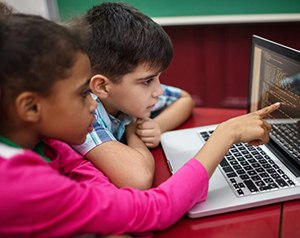 Girl pointing at computer screen learning coding next to boy